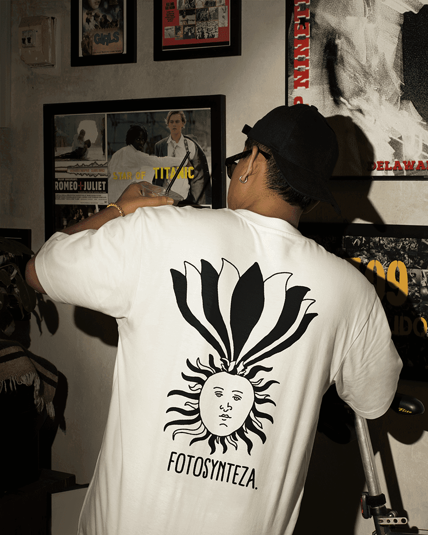 Młody mężczyzna w białej koszulce z nadrukiem słońca i napisem FOTOSYNTEZA